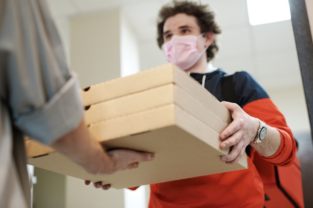 Delivery worker handing over pizzas while wearing a protective mask indoors, illustrating safe delivery practices during a pandemic.